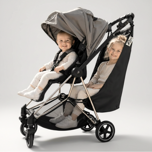 Two children sitting in a black and gray stroller with the stroller sling all-weather edition on a light gray background
